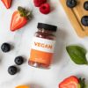 A flat lay of vegan supplements surrounded by fresh fruits on a white marble surface.