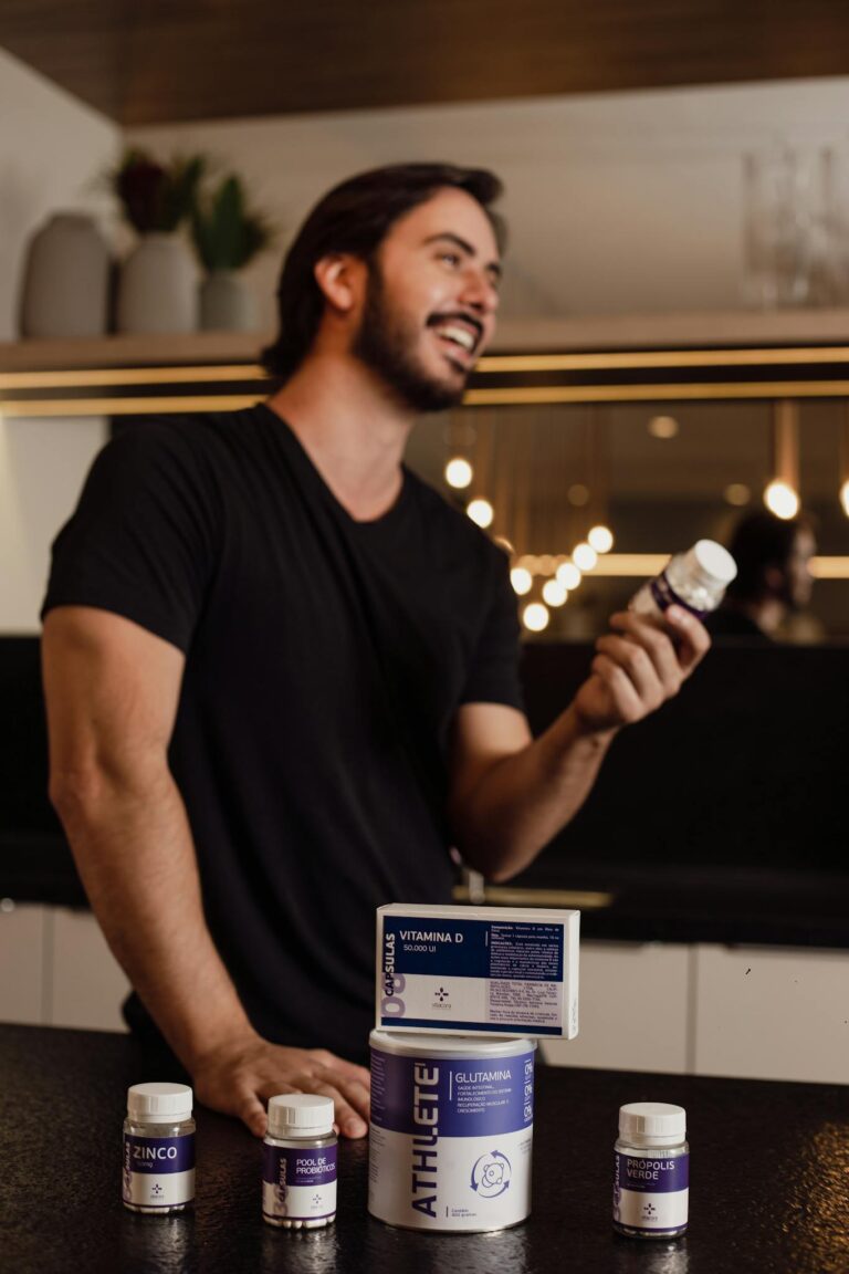 Adult male posing with various health supplements in a stylish kitchen setting.