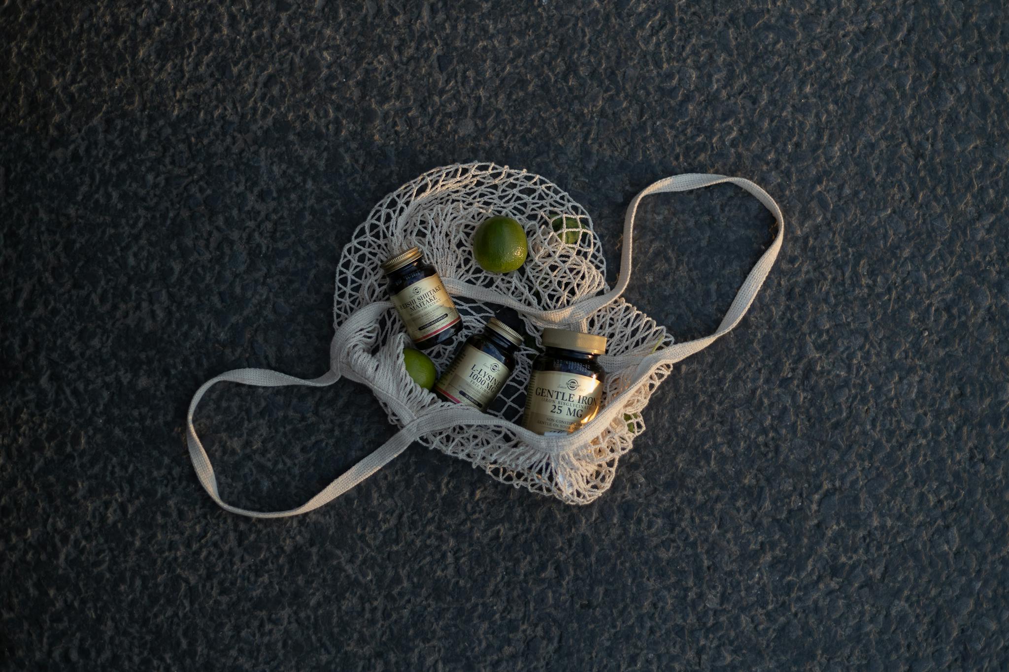 Top view of mineral supplement bottles in a mesh bag with limes on textured surface.